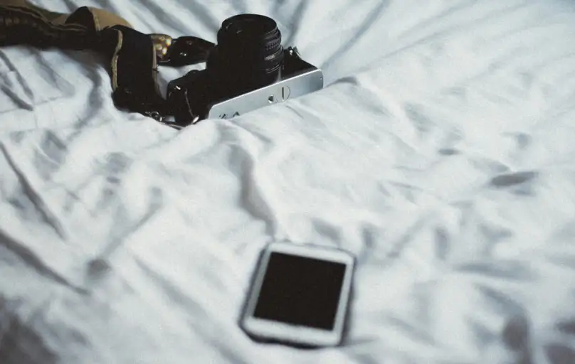 Aparat fotograficzny i smartfon leżące na białej pościeli