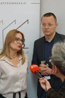 Prelegentka udziela wywiadu dla radia na tle ścianki Stowarzyszenia KAS