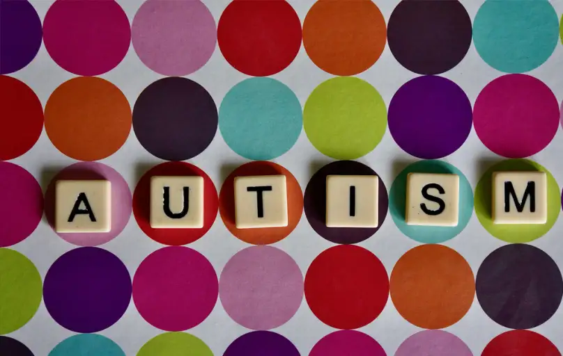 Płytki z literami układające słowo AUTISM na tle kolorowych kół
